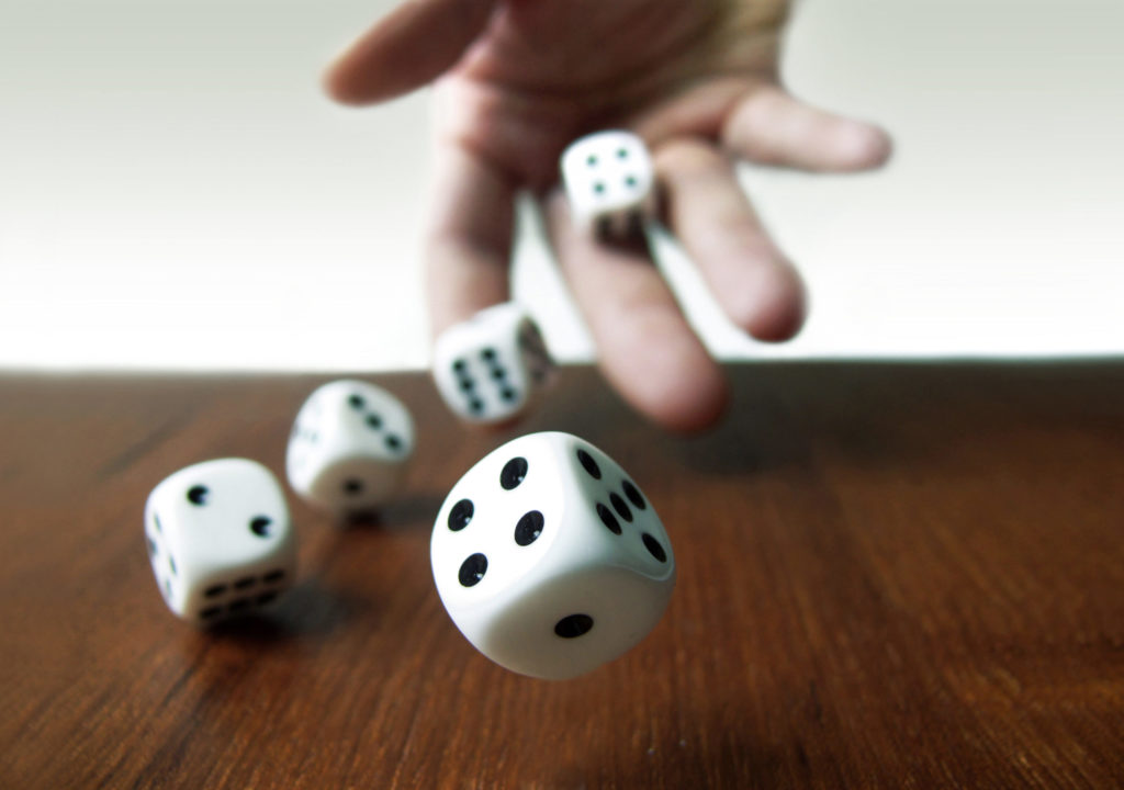 Hand rolling two dice on a wooden desk against a white background. 