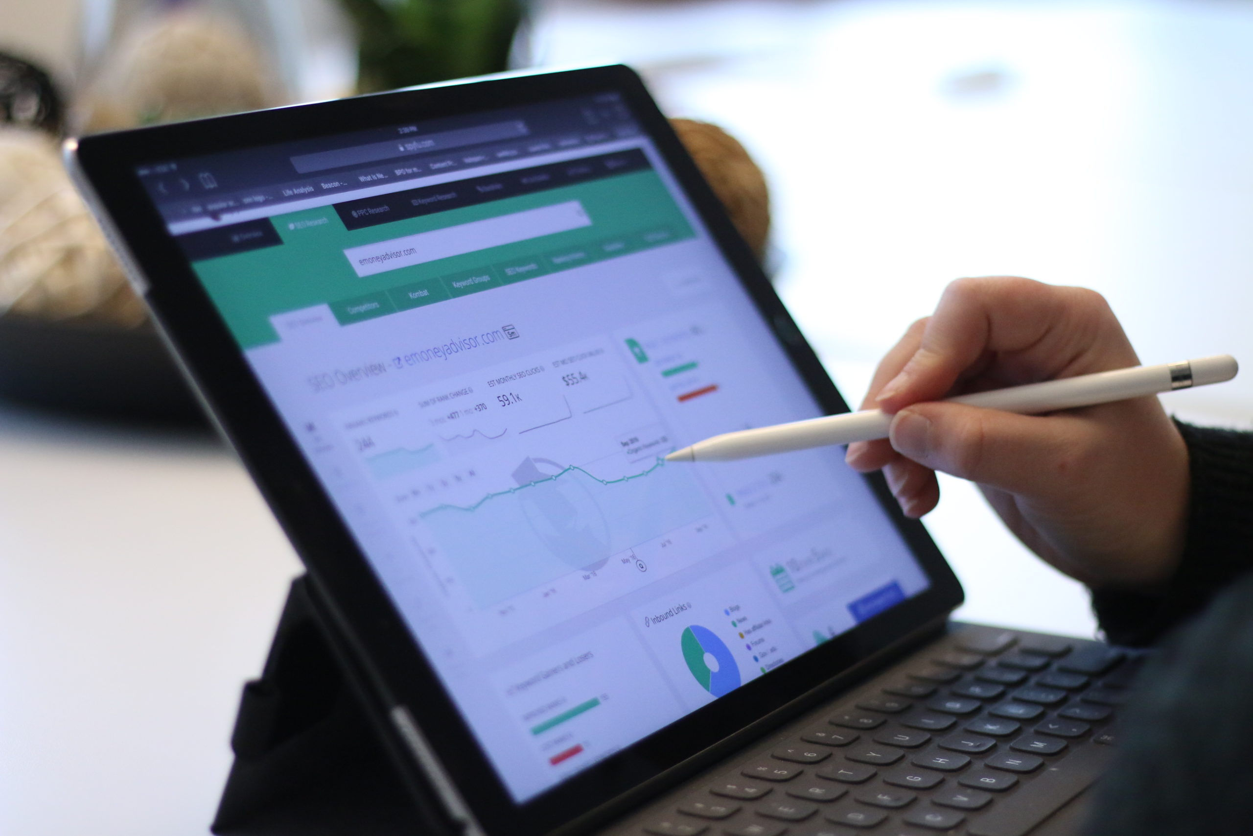 Side view of hand holding stylus pointing on laptop with graphs and charts on the screen.