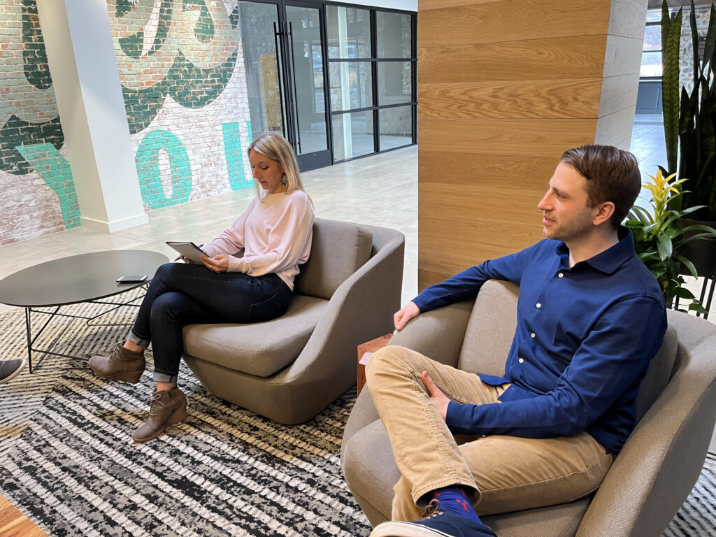 A man and woman sit in chairs in the Farotech office and discuss marketing strategy.
